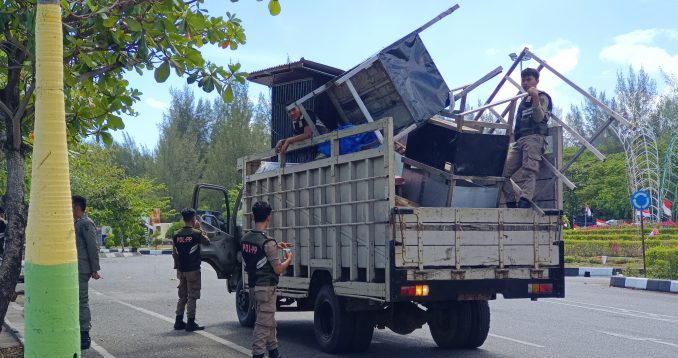 SITA BARANG PKL: Sejumlah personel Satpol PP WH Kota Banda Aceh mengangkut puluhan perlengkapan dagang milik PKL ke atas truk bak terbuka di sepanjang Jalan Syiah Kuala, Kecamatan Kuta Alam, Jumat (27/3/2026). Tindakan tegas ini dilakukan setelah para pedagang membiarkan barang-barang tersebut telantar di atas drainase usai bulan Ramadan, sehingga menciptakan kekumuhan dan melanggar ketertiban umum.