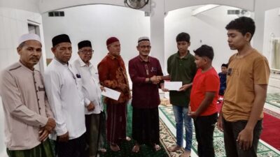 Penyerahan santunan anak yatim secara simbolis oleh tokoh masyarakat Leu Ue, Irwan Efendi Lubis, pada peringatan Nuzulul Qur'an di Meunasah Gampong Leu Ue, Darul Imarah, Aceh Besar, Sabtu (14/3/2026).